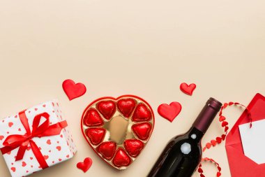 Sevgililer Günü için renkli arka planda bir şişe kırmızı şarap hediye kutusu, zarf ve çikolatalı. Kalp, hediye kutusuyla şekillendirilmiş çikolatalar fotokopi alanı ile üst görünüm.
