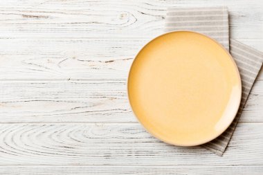 Renkli arka planda üst manzara. Yemek için masa örtüsü üzerinde boş yuvarlak sarı tabak. Tasarımınız için boşluk olan peçeteye boş tabak.