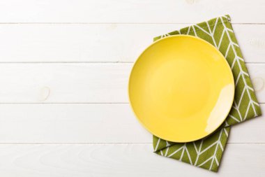 Renkli arka planda üst manzara. Yemek için masa örtüsü üzerinde boş yuvarlak sarı tabak. Tasarımınız için boşluk olan peçeteye boş tabak.