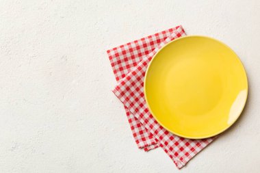 Renkli arka planda üst manzara. Yemek için masa örtüsü üzerinde boş yuvarlak sarı tabak. Tasarımınız için boşluk olan peçeteye boş tabak.