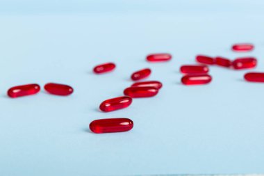 Renkli arka planda bir yığın kırmızı hap. Tabletler masaya saçılmış. Kırmızı yumuşak jelatin kapsül yığını. Vitaminler ve beslenme takviyeleri konsepti.