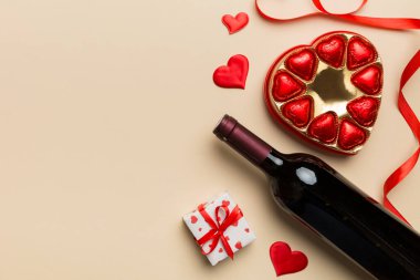 Sevgililer Günü için renkli arka planda bir şişe kırmızı şarap hediye ve çikolatalı. Kalp, hediye kutusuyla şekillendirilmiş çikolatalar fotokopi alanı ile üst görünüm.