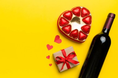 Sevgililer Günü için renkli arka planda bir şişe kırmızı şarap hediye ve çikolatalı. Kalp, hediye kutusuyla şekillendirilmiş çikolatalar fotokopi alanı ile üst görünüm.