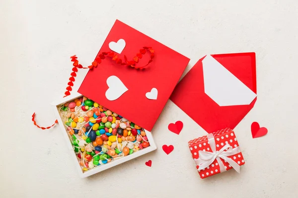 Red envelope with candy and gift box and Valentines hearts on colored background. Flat lay, top view. Romantic love letter for Holiday concept.