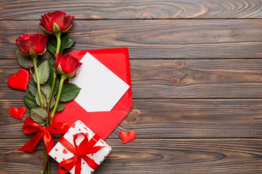 Zarflı sevgililer günü kompozisyonu, gül çiçeği ve kırmızı kalp masada. Üst manzara, düz yatış. Tatil kavramı.
