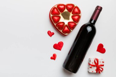 Sevgililer Günü için renkli arka planda bir şişe kırmızı şarap hediye ve çikolatalı. Kalp, hediye kutusuyla şekillendirilmiş çikolatalar fotokopi alanı ile üst görünüm.