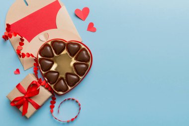 Sevgililer Günü için renkli arka planda hediye kutusu ve çikolatalı zarf. Kalp, hediye kutusuyla şekillendirilmiş çikolatalar fotokopi alanı ile üst görünüm.