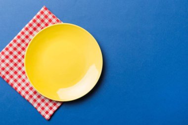 Renkli arka planda üst manzara. Yemek için masa örtüsü üzerinde boş yuvarlak sarı tabak. Tasarımınız için boşluk olan peçeteye boş tabak.