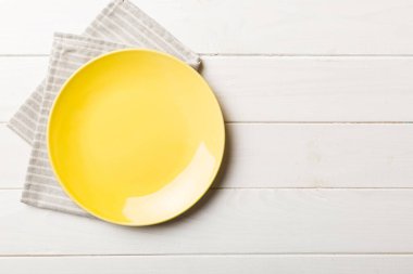 Renkli arka planda üst manzara. Yemek için masa örtüsü üzerinde boş yuvarlak sarı tabak. Tasarımınız için boşluk olan peçeteye boş tabak.