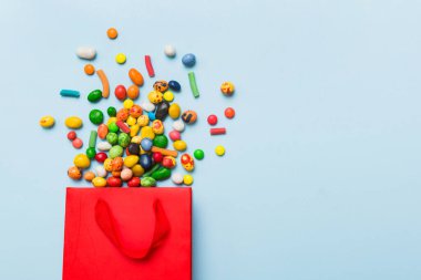 shopping paper gift bag in corner full of assorted traditional candies falling out on colored background with copy space. Happy Holidays sale concept.