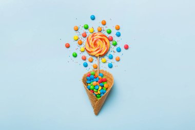 waffle cone full of assorted traditional candies falling out on colored background with copy space. Happy Holidays sale concept.