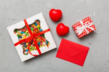 Red envelope with candy and gift box and Valentines hearts on colored background. Flat lay, top view. Romantic love letter for Holiday concept.