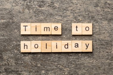 Tahta bloğa yazılmış tatil kelimesi zamanı. Çimento masasındaki tatil metninin zamanı geldi..