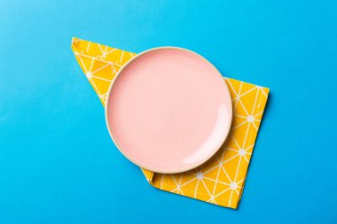 Renkli arka planda üst manzara. Yemek için masa örtüsü üzerine yuvarlak pembe tabak. Tasarımınız için boşluk olan peçeteye boş tabak.