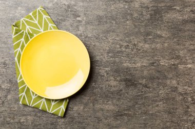 Renkli arka planda üst manzara. Yemek için masa örtüsü üzerinde boş yuvarlak sarı tabak. Tasarımınız için boşluk olan peçeteye boş tabak.