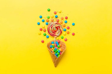 waffle cone full of assorted traditional candies falling out on colored background with copy space. Happy Holidays sale concept.