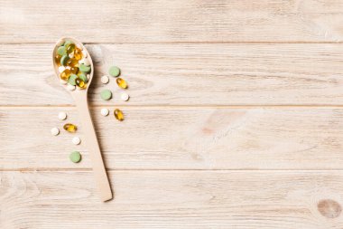 Renkli bir arka planda tahta kaşıkta vitamin kapsülleri. Haplar sağlıklı bir yemek olarak sunuldu. Uyuşturucu, eczane, ilaç veya sağlık hizmetleri kavramı.