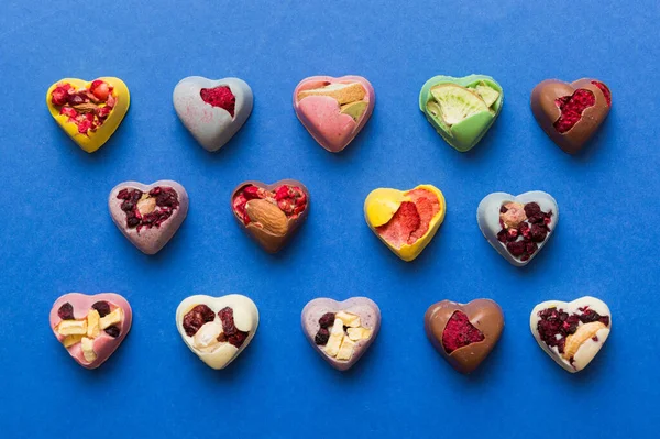 chocolate sweets in the form of a heart with fruits and nuts on a colored background. top view with space for text, holiday concept.