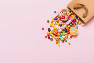 shopping paper gift bag in corner full of assorted traditional candies falling out on colored background with copy space. Happy Holidays sale concept.