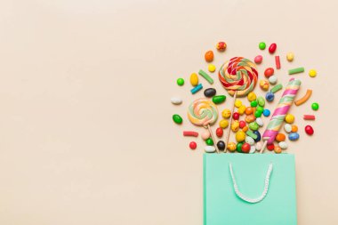 shopping paper gift bag in corner full of assorted traditional candies falling out on colored background with copy space. Happy Holidays sale concept.