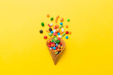 waffle cone full of assorted traditional candies falling out on colored background with copy space. Happy Holidays sale concept.