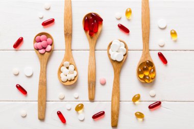 Renkli bir arka planda kaşıkta vitamin kapsülleri. Haplar sağlıklı bir yemek olarak sunuldu. Kırmızı yumuşak jel vitamin takviye kapsülleri kaşık üzerinde.