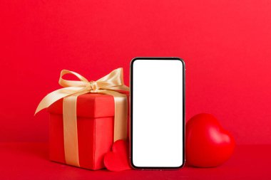 mobile phone with blank screen on colored background with hearts, calendar and gift box, valentine day concept perspertive view flat lay.