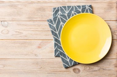 Renkli arka planda üst manzara. Yemek için masa örtüsü üzerinde boş yuvarlak sarı tabak. Tasarımınız için boşluk olan peçeteye boş tabak.