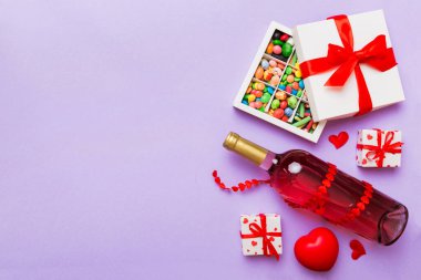 Sevgililer Günü için renkli arka planda bir şişe kırmızı şarap hediye ve çikolatalı. Kalp, hediye kutusuyla şekillendirilmiş çikolatalar fotokopi alanı ile üst görünüm.