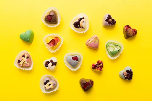 chocolate sweets in the form of a heart with fruits and nuts on a colored background. top view with space for text, holiday concept.