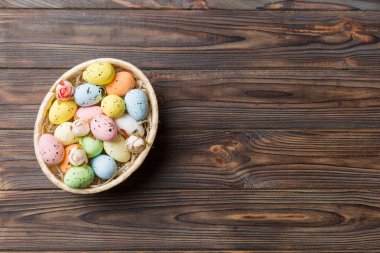 Colorful Easter eggs in wicker basket against colored background, closeup. top view with copy space.