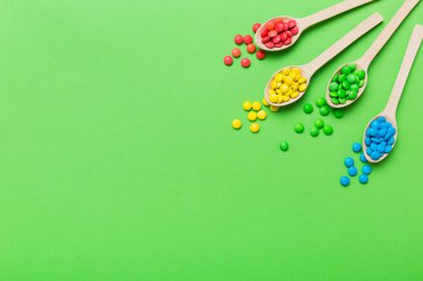 Renkli arka planda kaşık üzerinde renkli tatlı şekerler. Fotokopi alanı ile şekerleme dekoru üst görünümü.