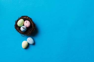 Colorful easter eggs in nest on table background with copy space top view.
