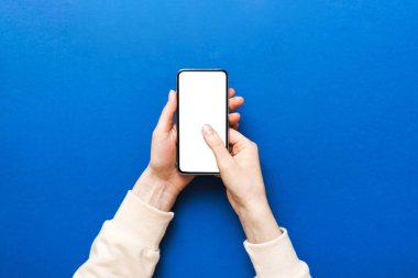 Mesajınız veya bilgi içeriğiniz için boş bir kopya ekranı olan akıllı telefonları tutan kadın ellerinin üst görünümü. üst görünümde telefon beyaz ekranı kullanan kadın eli.