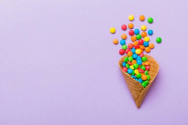 waffle cone full of assorted traditional candies falling out on colored background with copy space. Happy Holidays sale concept.