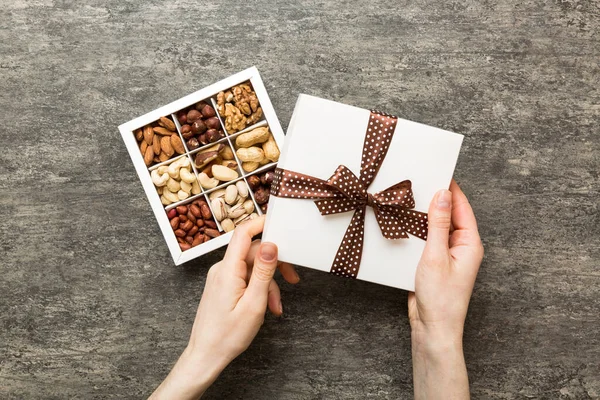 Young woman holding box with different nuts, closeup. Close up, copy space, top view, flat lay. Walnut, pistachios, almonds, hazelnuts and cashews.