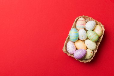 Colorful Easter eggs in wicker basket against colored background, closeup. top view with copy space.