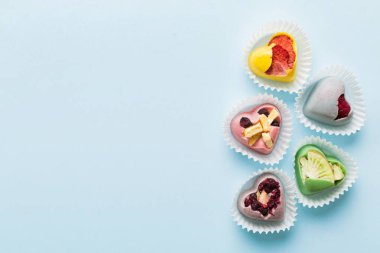 chocolate sweets in the form of a heart with fruits and nuts on a colored background. top view with space for text, holiday concept.