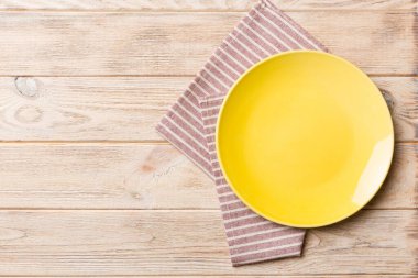 Renkli arka planda üst manzara. Yemek için masa örtüsü üzerinde boş yuvarlak sarı tabak. Tasarımınız için boşluk olan peçeteye boş tabak.