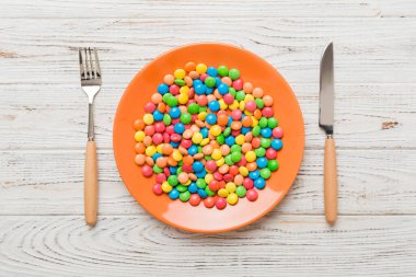 cutlery on table and sweet plate of candy. Health and obesity concept, top view on colored background.