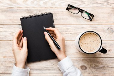 Not defterine kalem yazan ve kahve bardağını tutan kadın eli. Kahve masasında çalışan bir kadın..