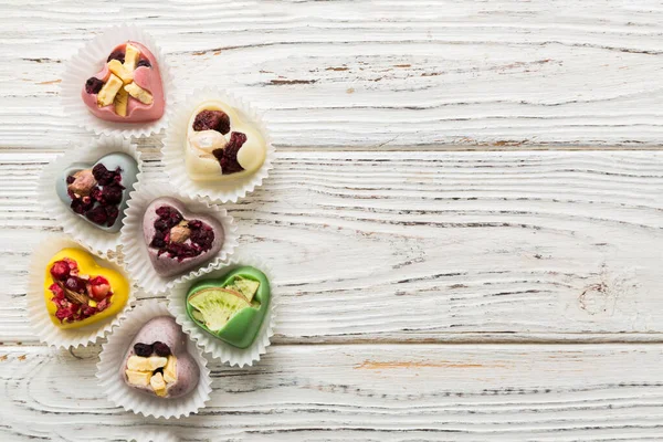 stock image chocolate sweets in the form of a heart with fruits and nuts on a colored background. top view with space for text, holiday concept.