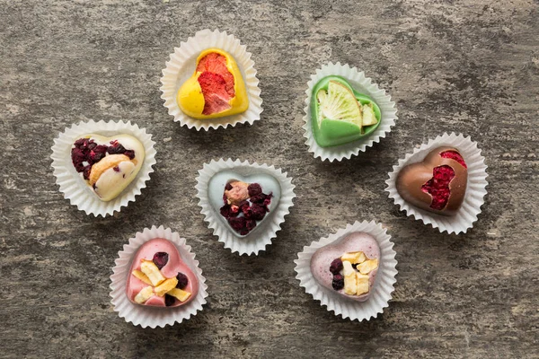 stock image chocolate sweets in the form of a heart with fruits and nuts on a colored background. top view with space for text, holiday concept.