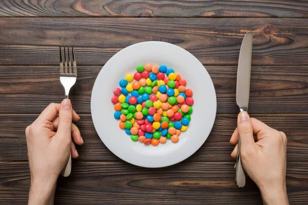 the girl holds cutlery in her hands and eats sweets in a plate. Health and obesity concept, top view on colored background.