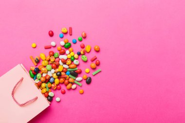 shopping paper gift bag in corner full of assorted traditional candies falling out on colored background with copy space. Happy Holidays sale concept.