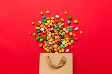 shopping paper gift bag in corner full of assorted traditional candies falling out on colored background with copy space. Happy Holidays sale concept.