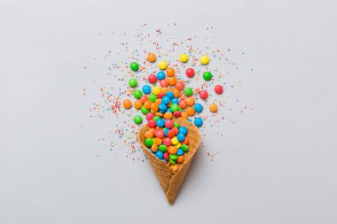 waffle cone full of assorted traditional candies falling out on colored background with copy space. Happy Holidays sale concept.