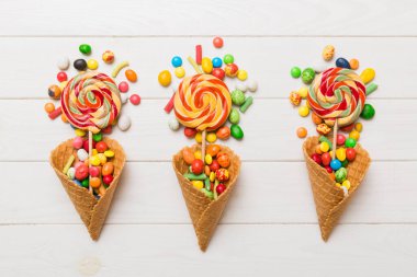 waffle cone full of assorted traditional candies falling out on colored background with copy space. Happy Holidays sale concept.