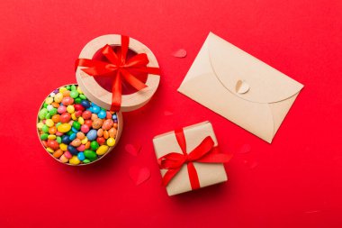 Red envelope with candy and gift box and Valentines hearts on colored background. Flat lay, top view. Romantic love letter for Holiday concept.