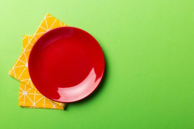 Renkli arka planda üst görünüm yiyecek için masa örtüsü üzerindeki boş yuvarlak kırmızı tabak. Tasarımınız için boşluk olan peçeteye boş tabak.